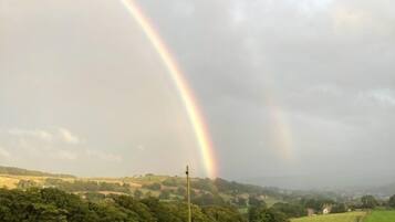 A rural landscape with a stone wall and a rainbow in the sky.
