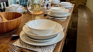 Une longue table à manger, dressée avec de l’assiette blanche, des bols et des couverts, un saladier en bois et un vase rempli de fleurs jaunes.