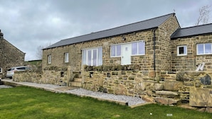 Un bâtiment en pierre avec un toit en pente, une allée gravillonnée et une pelouse verdoyante.