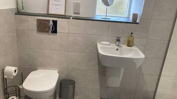A bathroom with a toilet, sink, and a window with a mirror. There is a sign on the wall and a trash can.
