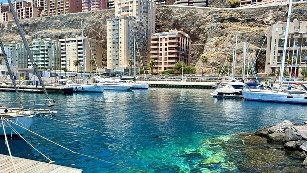 A marina with boats docked, clear water, and buildings in the background. - Apartment in Radazul with Stunning Sea Views (Radazul)