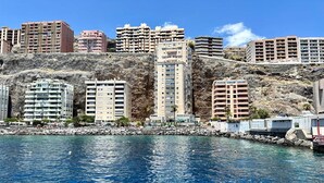 A coastal cityscape with high-rise buildings, a rocky hillside, and a clear blue sea. - Apartment in Radazul with Stunning Sea Views (Radazul)