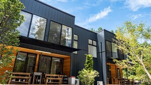 Un edificio moderno de dos pisos con amplias ventanas, terraza de madera y asientos al aire libre.