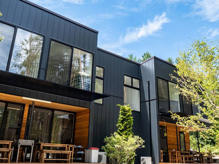 A modern two-story building with large windows, wooden deck, and outdoor seating.