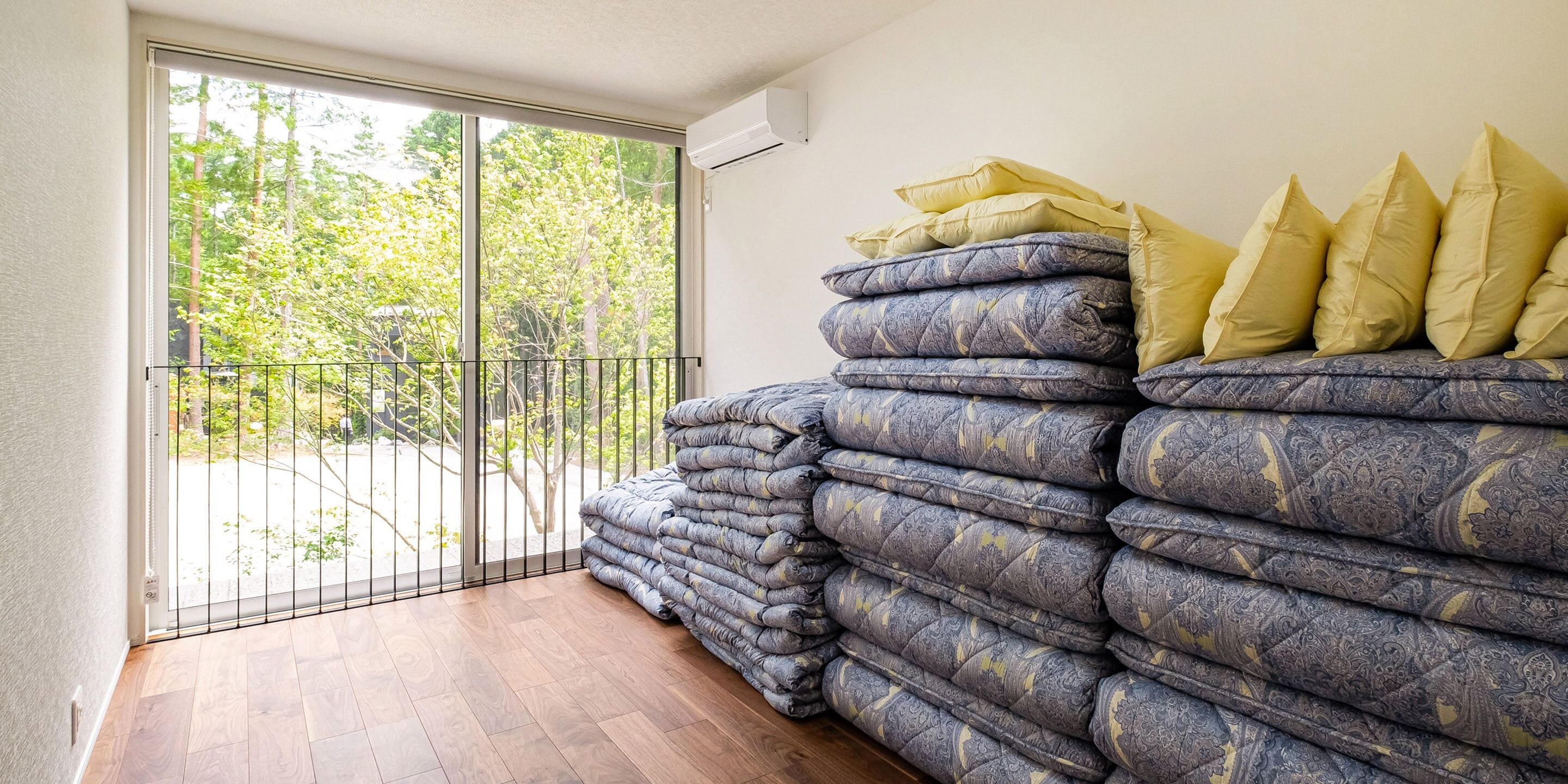 Ein Zimmer mit großem Fenster, einer Matratzenstapel und einer Geländer.