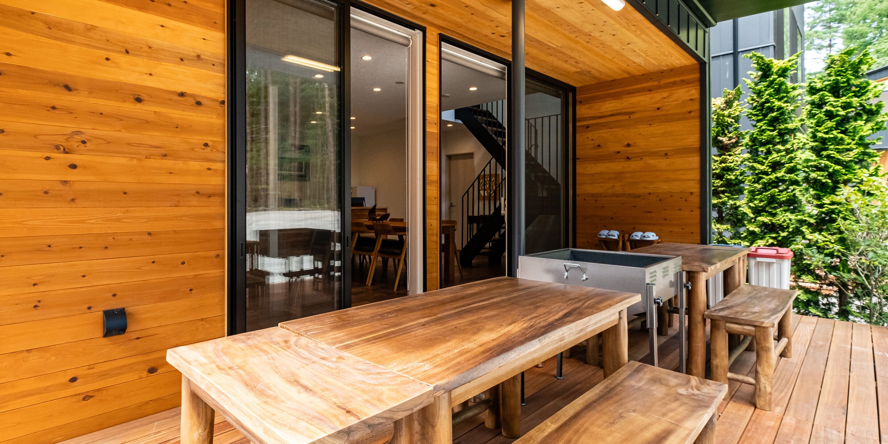 A wooden deck with a dining table and benches, a sliding glass door leading to an interior space, and a staircase.