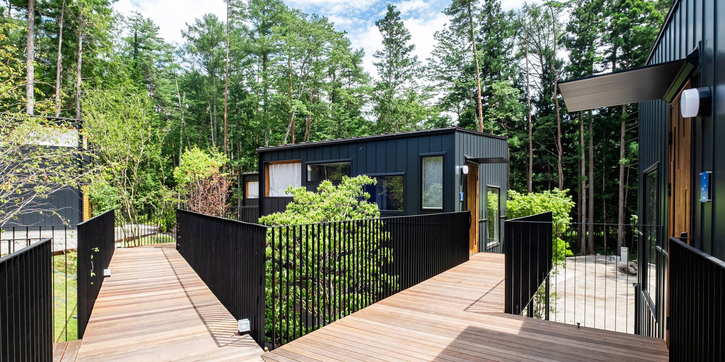 Een moderne cabin met een houten terras, omgeven door dicht bos.