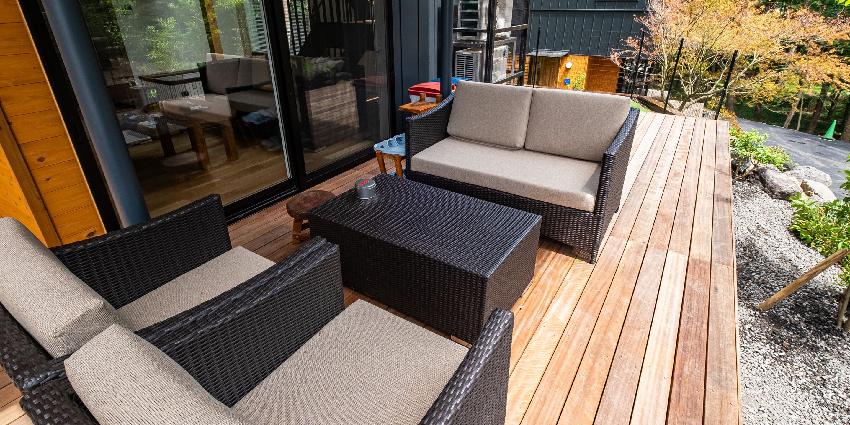 An outdoor patio with wicker furniture, a wooden deck, and a glass door leading to an interior space.
