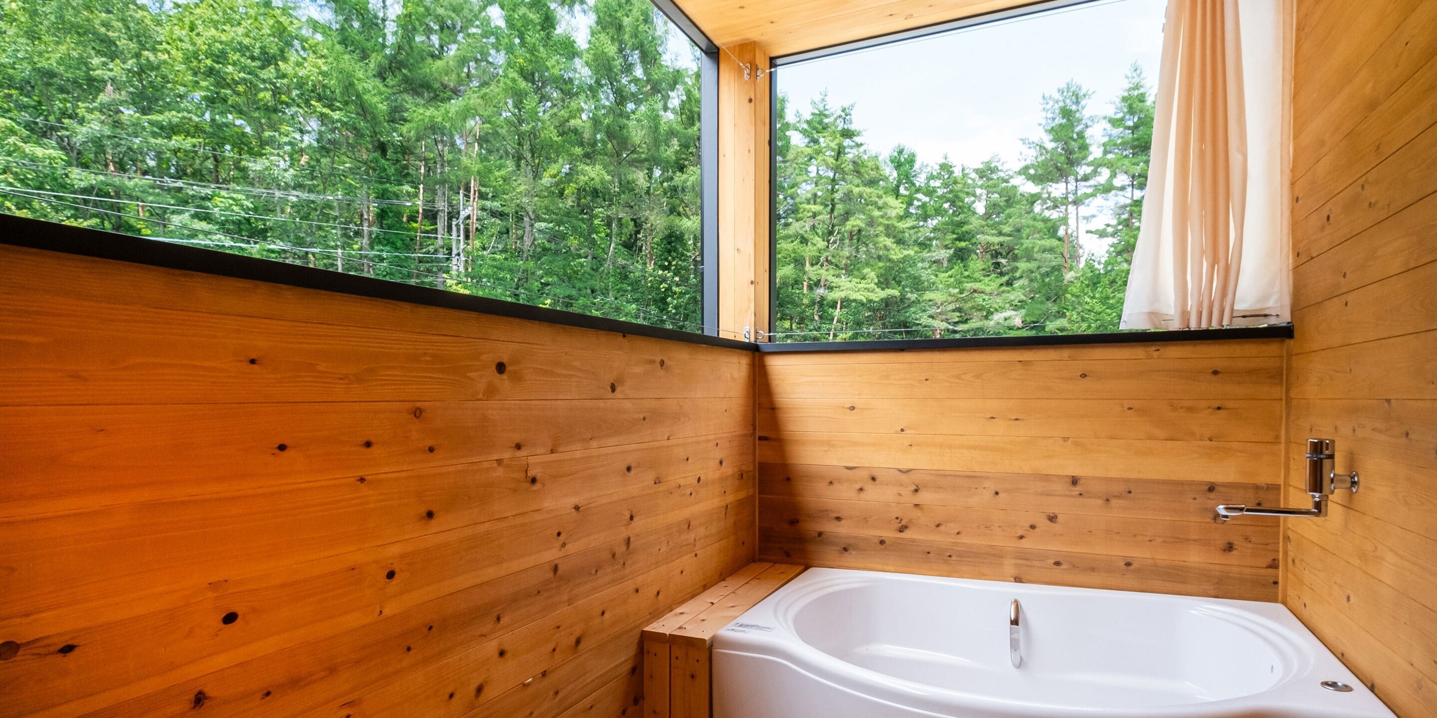 Una cabaña de madera con un ventanal grande, una bañera blanca y piso de madera.