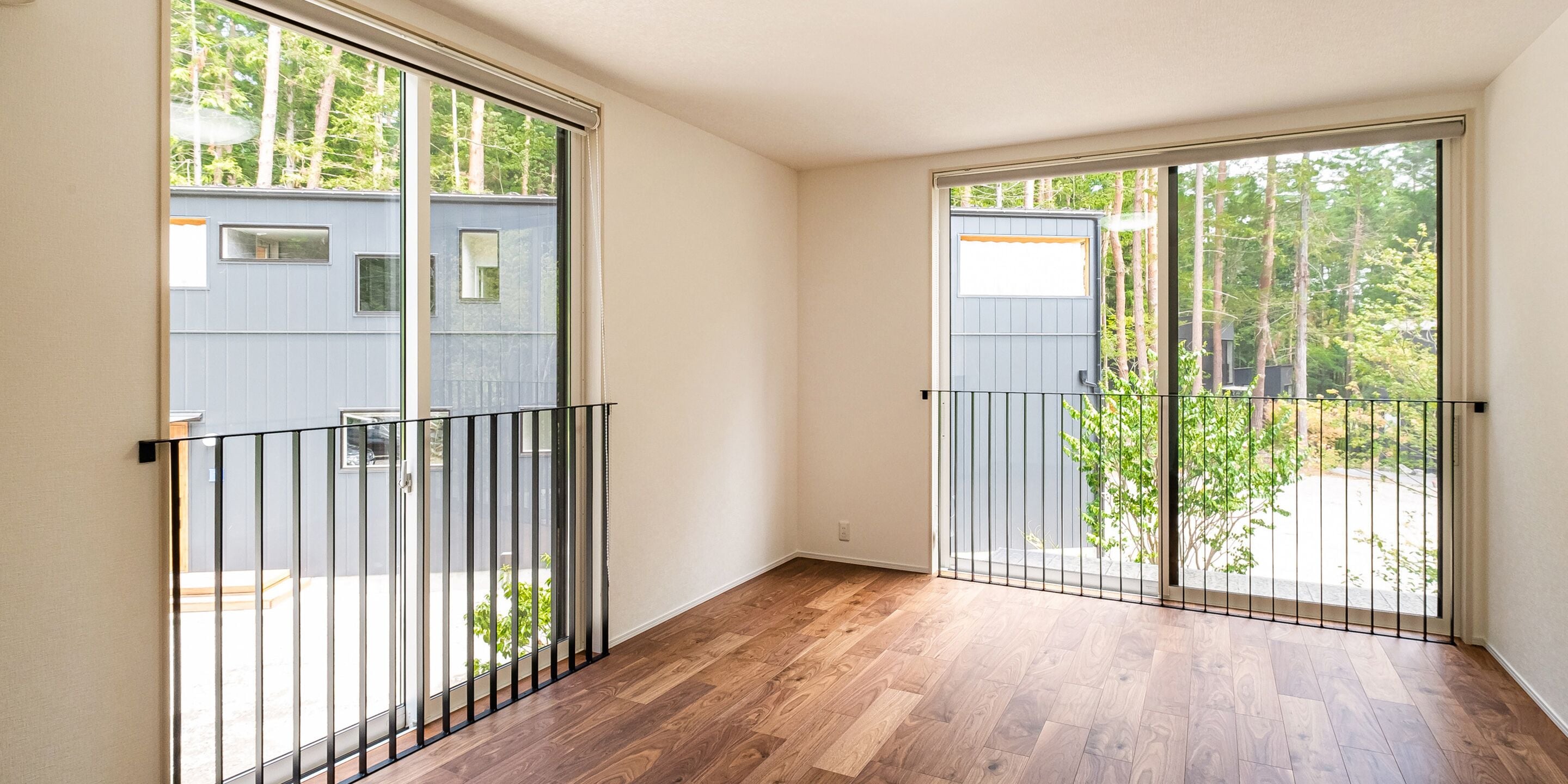 A room with a wooden floor, a sliding glass door leading to a balcony, and a view of trees and a building outside.