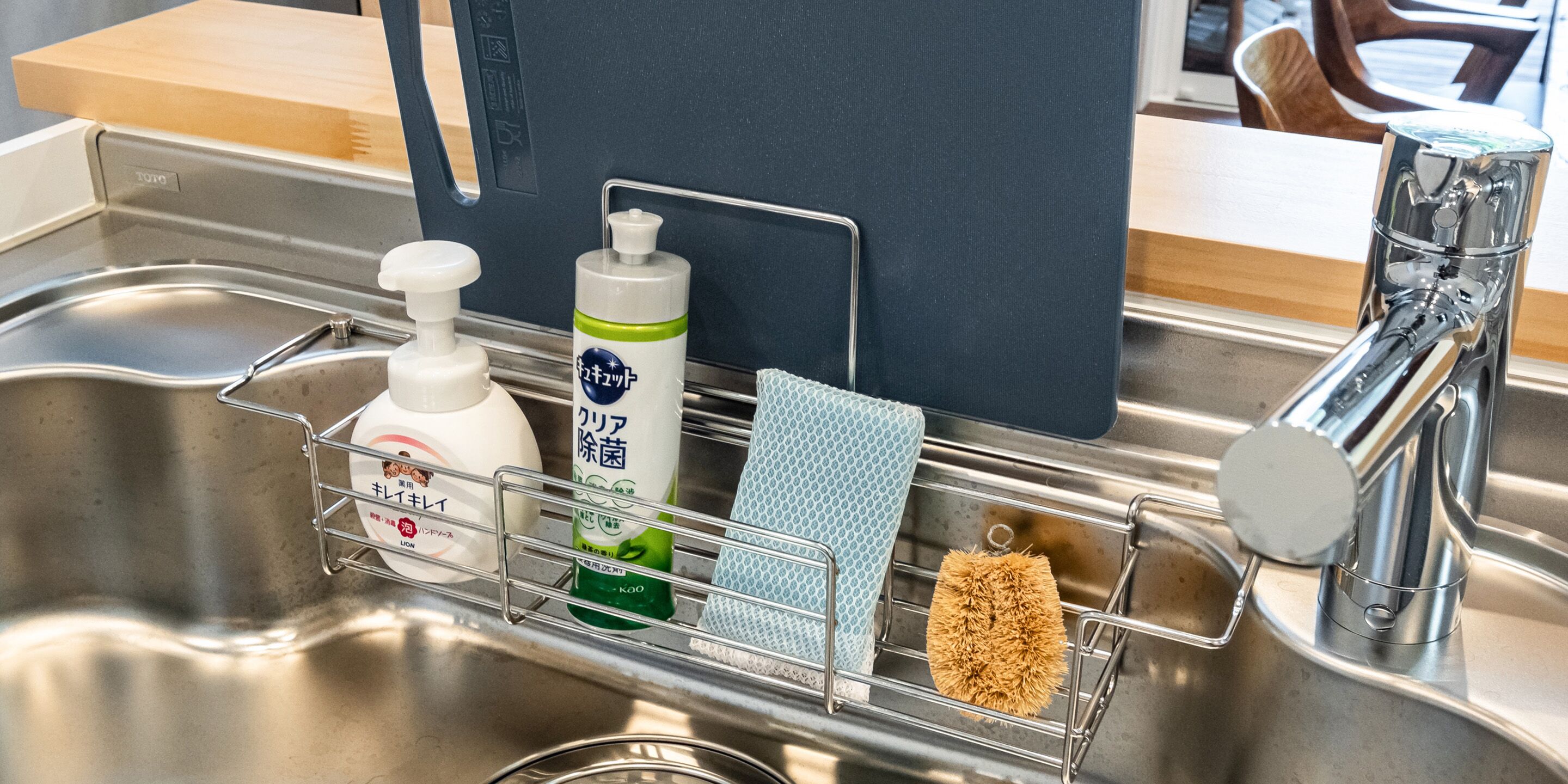 A kitchen sink with a stainless steel faucet, a soap dispenser, a bottle of dish soap, a sponge, and a dish rack.