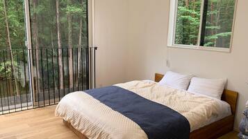 A bedroom with a bed, a window with a forest view, and a balcony with a railing.