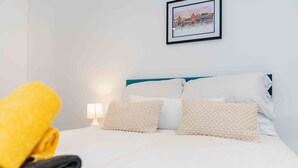 A neatly made bed with white and beige pillows, a blue headboard, and a framed picture on the wall. - Street View Modern Apartment (Hull)