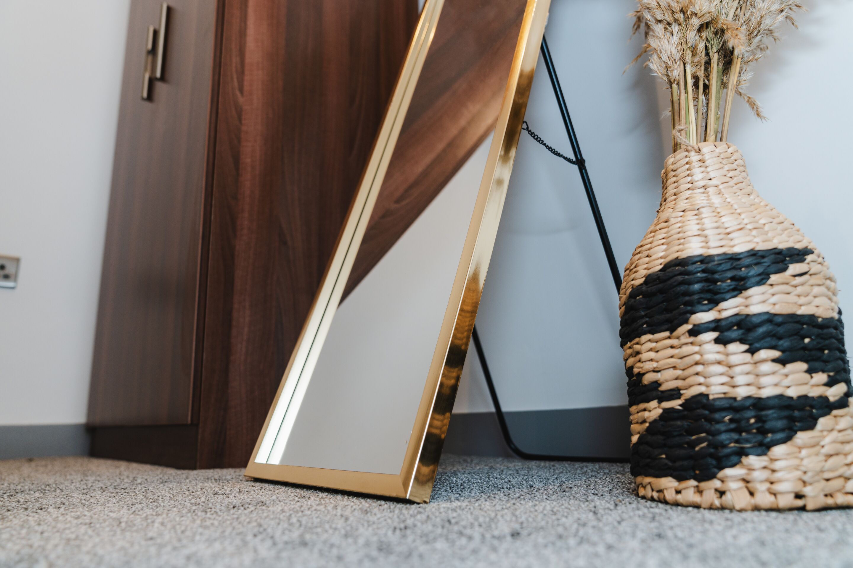 A framed picture leaning against a wooden door, a woven basket with dried plants, and a black cable on a carpeted floor.