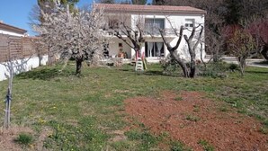 A two-story house with a tiled roof, surrounded by a grassy yard and trees. - LE Gîte LA Maison DE Papou Le Tilleul (Nans-les-Pins)