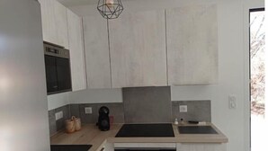 A modern kitchen with light wood cabinets, a black countertop, a built-in oven, and a hanging light fixture. - LE Gîte LA Maison DE Papou Le Tilleul (Nans-les-Pins)