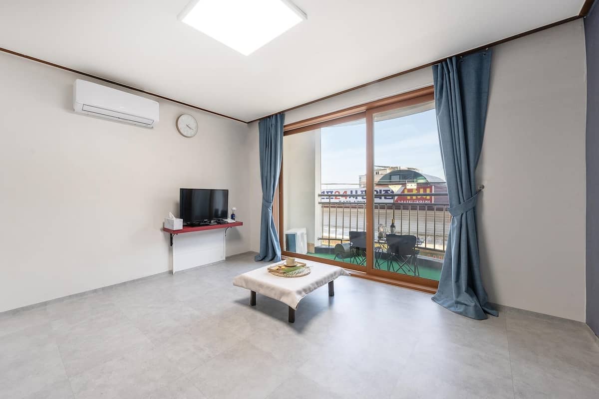 Ein modernes Wohnzimmer mit einem Flachbildfernseher, einem kleinen Tisch mit einer Snackplatte, einer Uhr und einem großen Fenster mit Vorhängen.