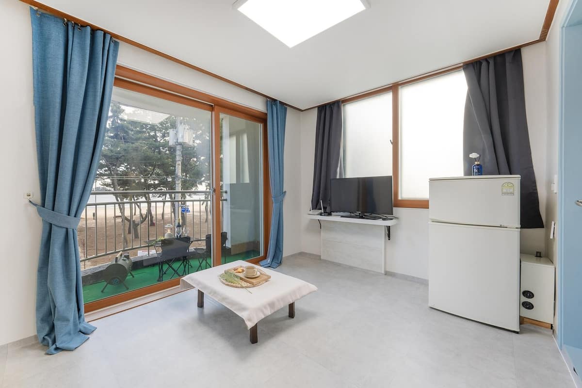 Ein kleines Zimmer mit Balkon, einem kleinen Tisch mit Tablett, einem Fernseher und einem Kühlschrank.
