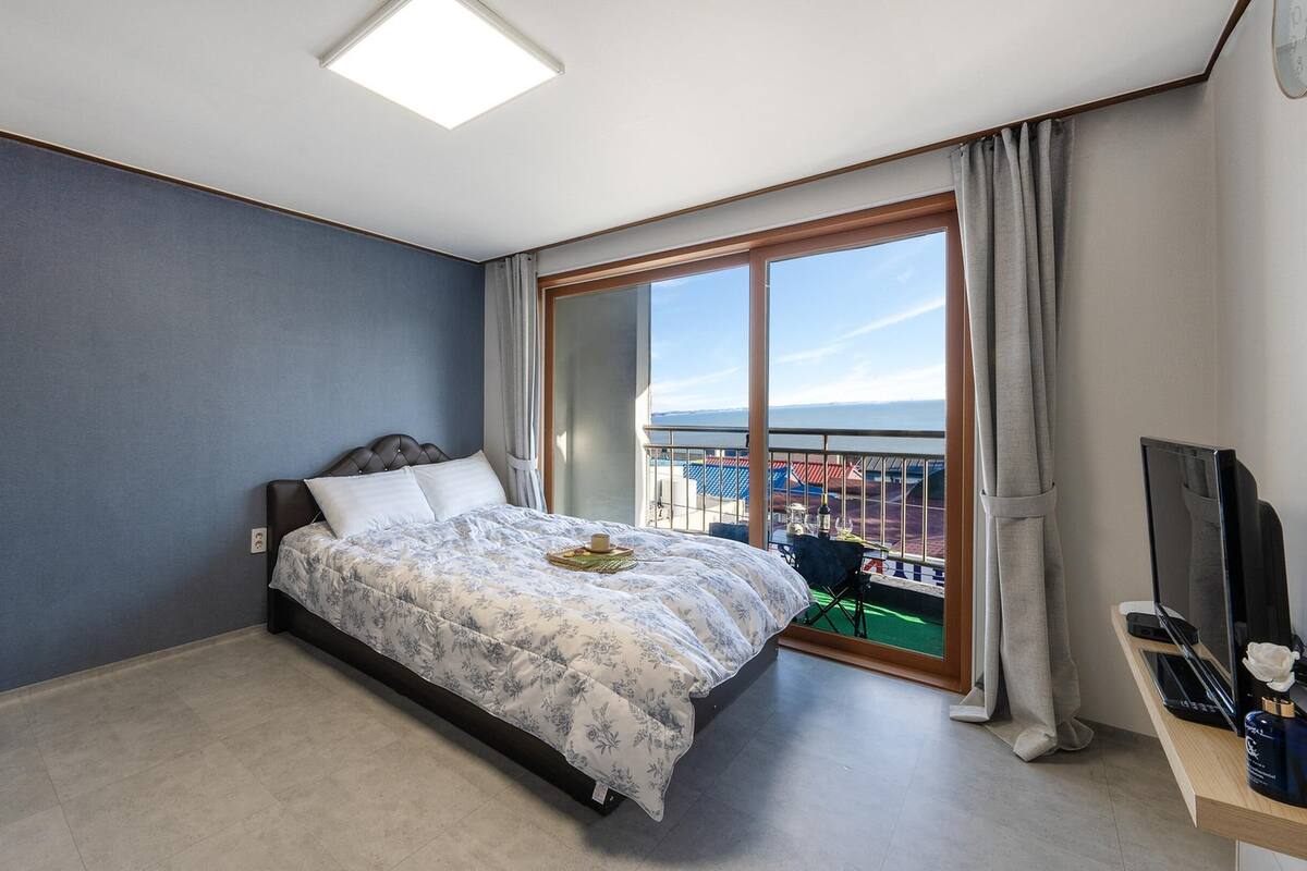 Ein modernes Schlafzimmer mit einem großen Bett, einem Fernseher und einem Balkon mit Blick auf die Stadt.