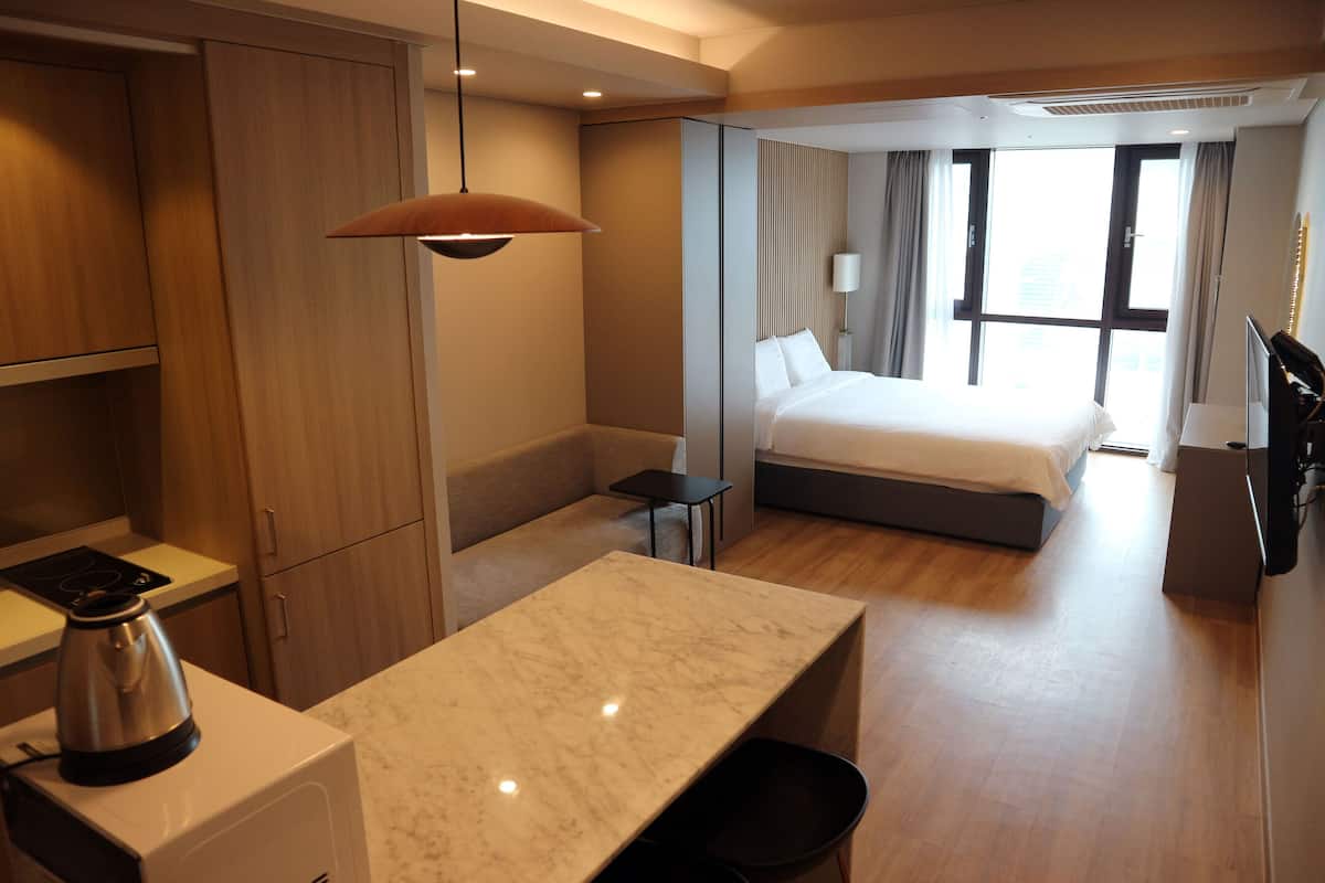 A hotel room with a bed, a desk, a kettle, and a view of the city.