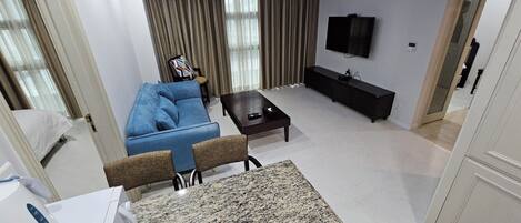 Una sala de estar moderna con un sofá azul, una mesa de centro, un televisor y una zona de cocina con encimera de granito.
