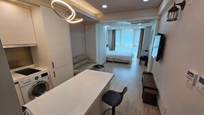 A compact hotel room with a kitchenette, a bed, a seating area, and a TV mounted on the wall. - W Residence Hotel Centum City (Busan)