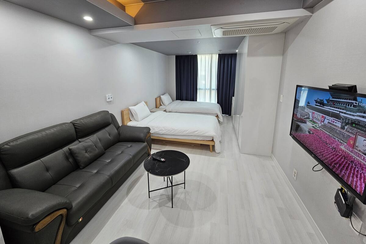 A modern hotel room with a sofa, two single beds, a TV, and a small table.