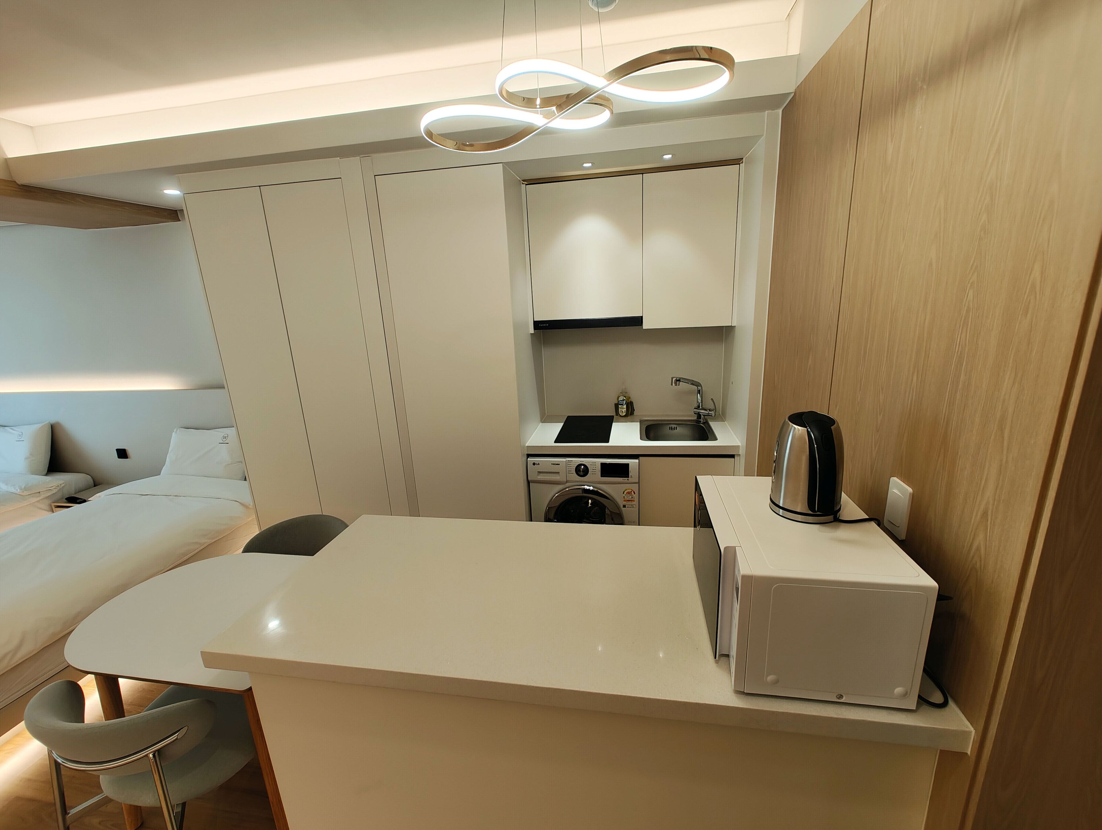 Een compacte hotelkamer met een bed, een klein kitchenette, een wasmachine en een koffiezetapparaat.