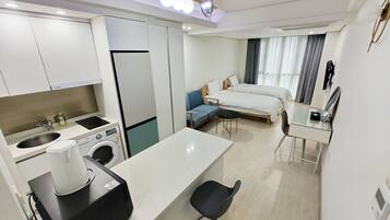 A modern hotel room with a kitchenette, a bed, a sofa, and a desk.