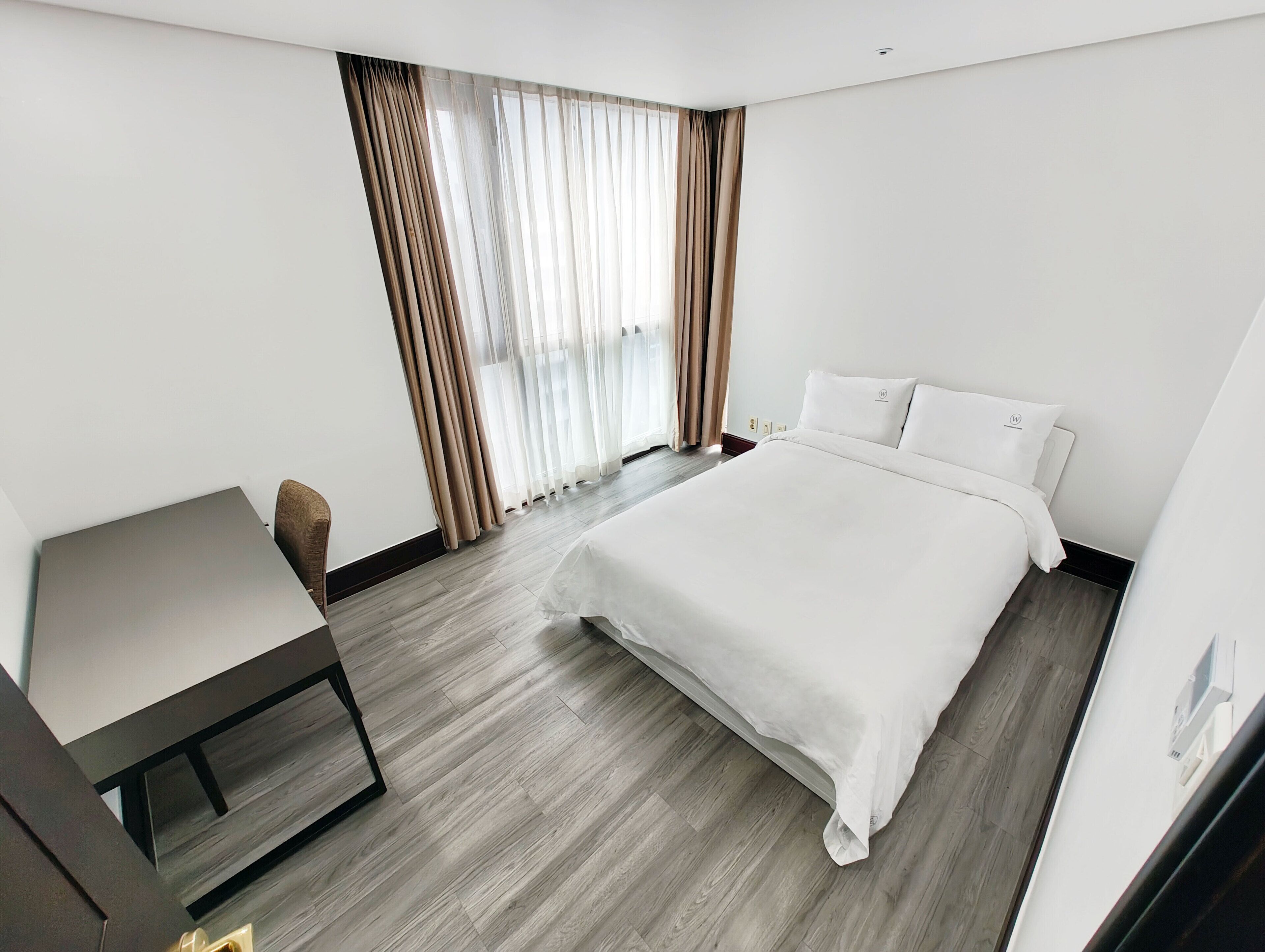 A modern hotel room with a large bed, a desk, and a chair.