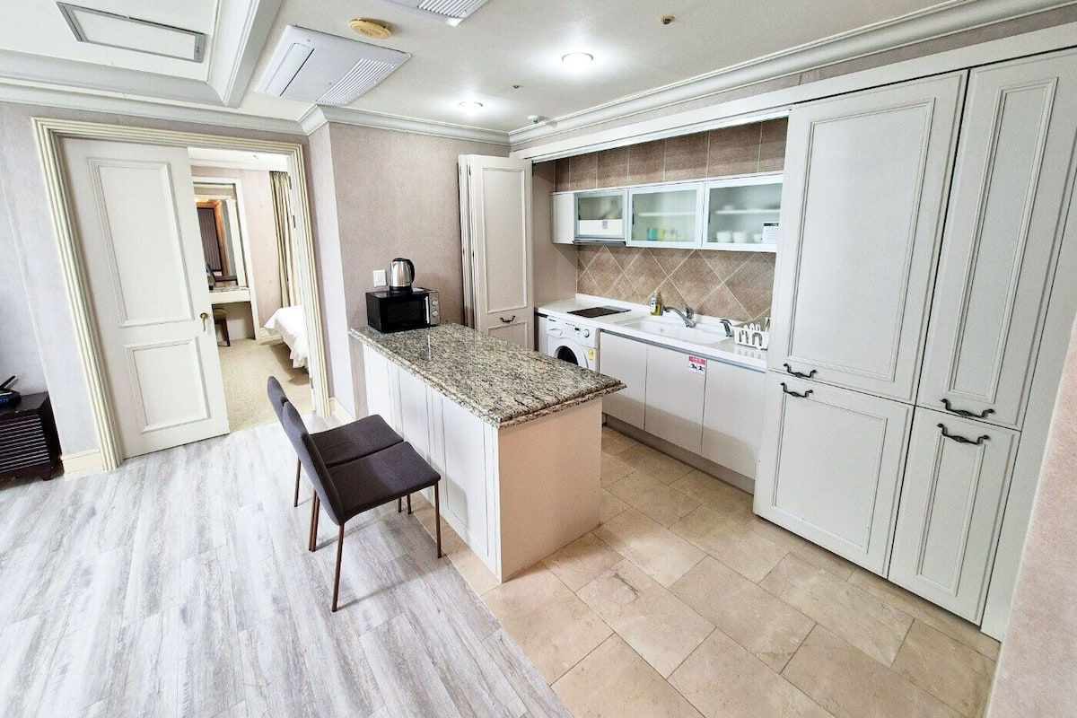 A compact kitchen with a granite countertop, white cabinets, a built-in microwave, and a sink.