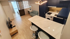 A modern kitchen with a built-in washing machine, a dining area with a wooden table, and a seating area with a sofa. - W Residence Hotel Centum City (Busan)