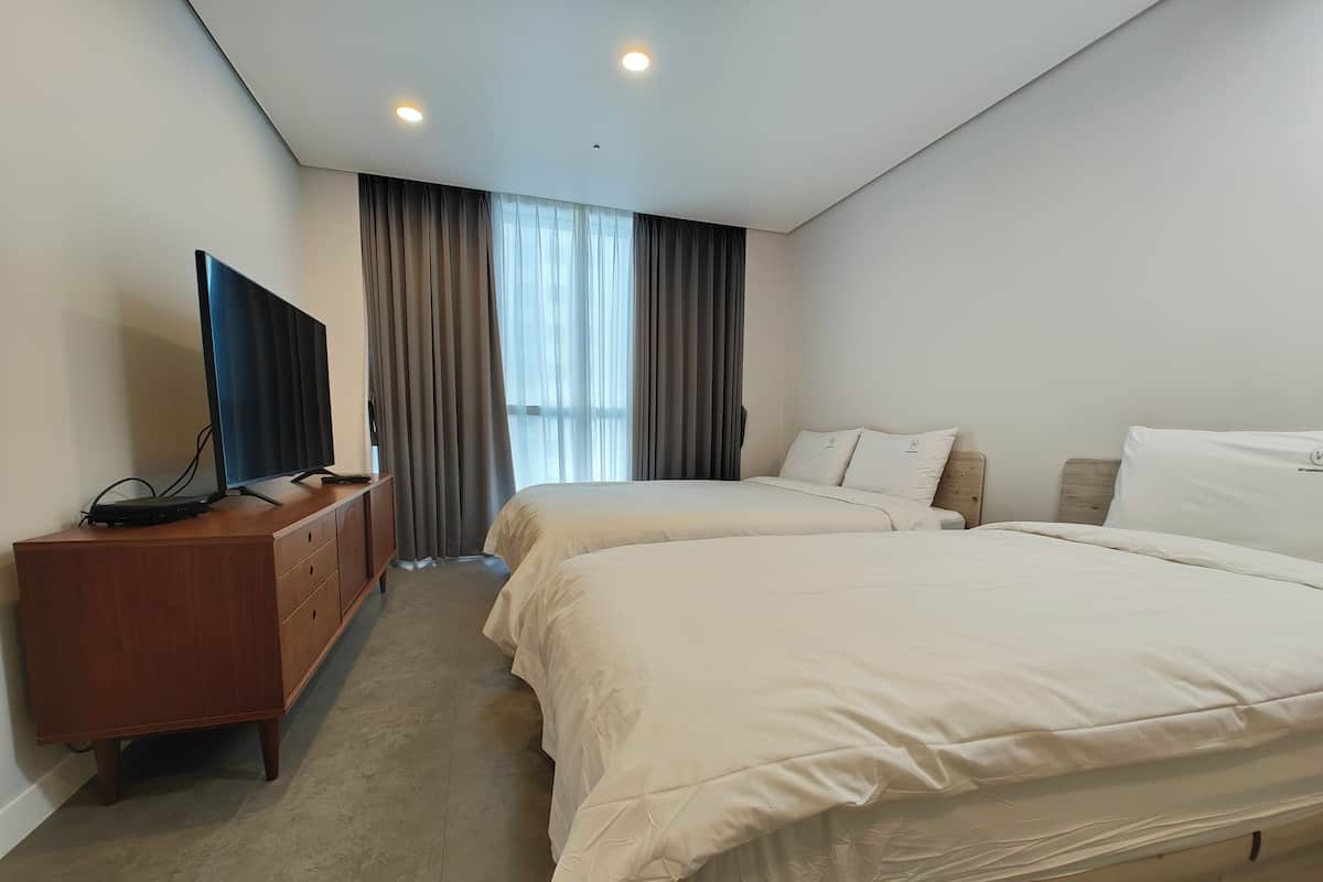 A hotel room with two beds, a TV on a wooden dresser, and a large window with curtains.