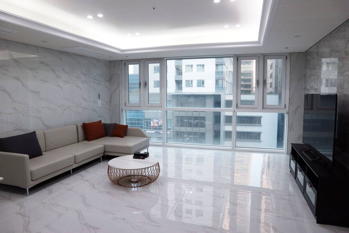 A modern living room with a sectional sofa, a round coffee table, and a large window offering a city view.