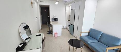 Una habitación moderna y bien iluminada con un escritorio de vidrio, un sofá azul y una pequeña mesa redonda.
