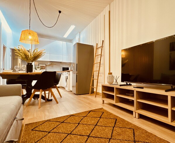 A modern living room with a TV, wooden entertainment unit, and a dining area with a table and chairs.
