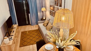 A modern living room with a sofa, a dining table set for two, a decorative lamp, and a view of the cityscape through the window. - Modern And Luxury Flat in Telde (Telde)