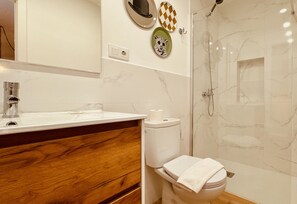 A bathroom with a wooden vanity, a toilet, a shower, and decorative wall art. - Modern And Luxury Flat in Telde (Telde)