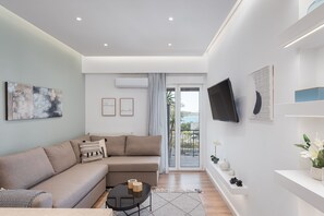 A modern living room with a sofa, a coffee table, and a TV mounted on the wall. There is a sliding glass door leading to a balcony. - Glyfada Cozy Living (Glyfada)