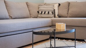 A living room with a grey sofa, patterned throw pillows, a small black coffee table, and a woven rug. - Glyfada Cozy Living (Glyfada)