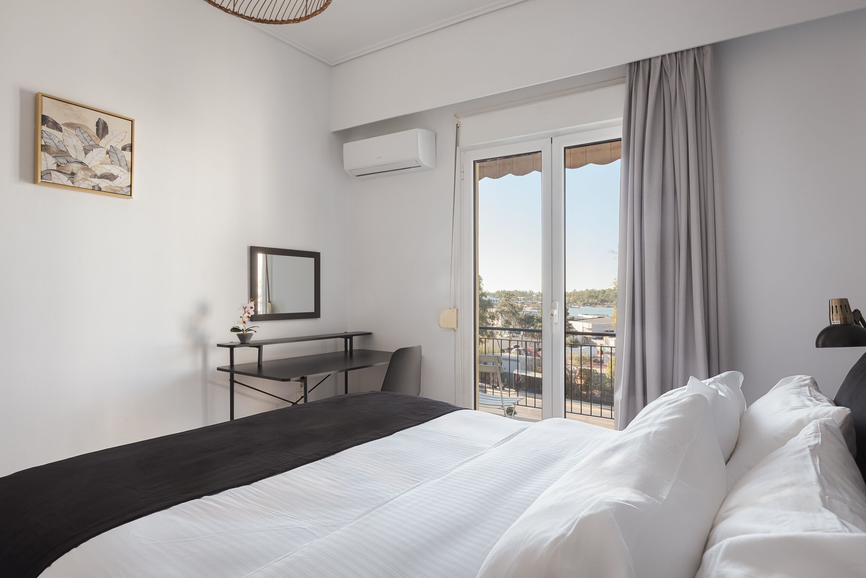 Ett hotellrum med en säng, ett skrivbord, en stol, en krukväxt och en balkong med utsikt.