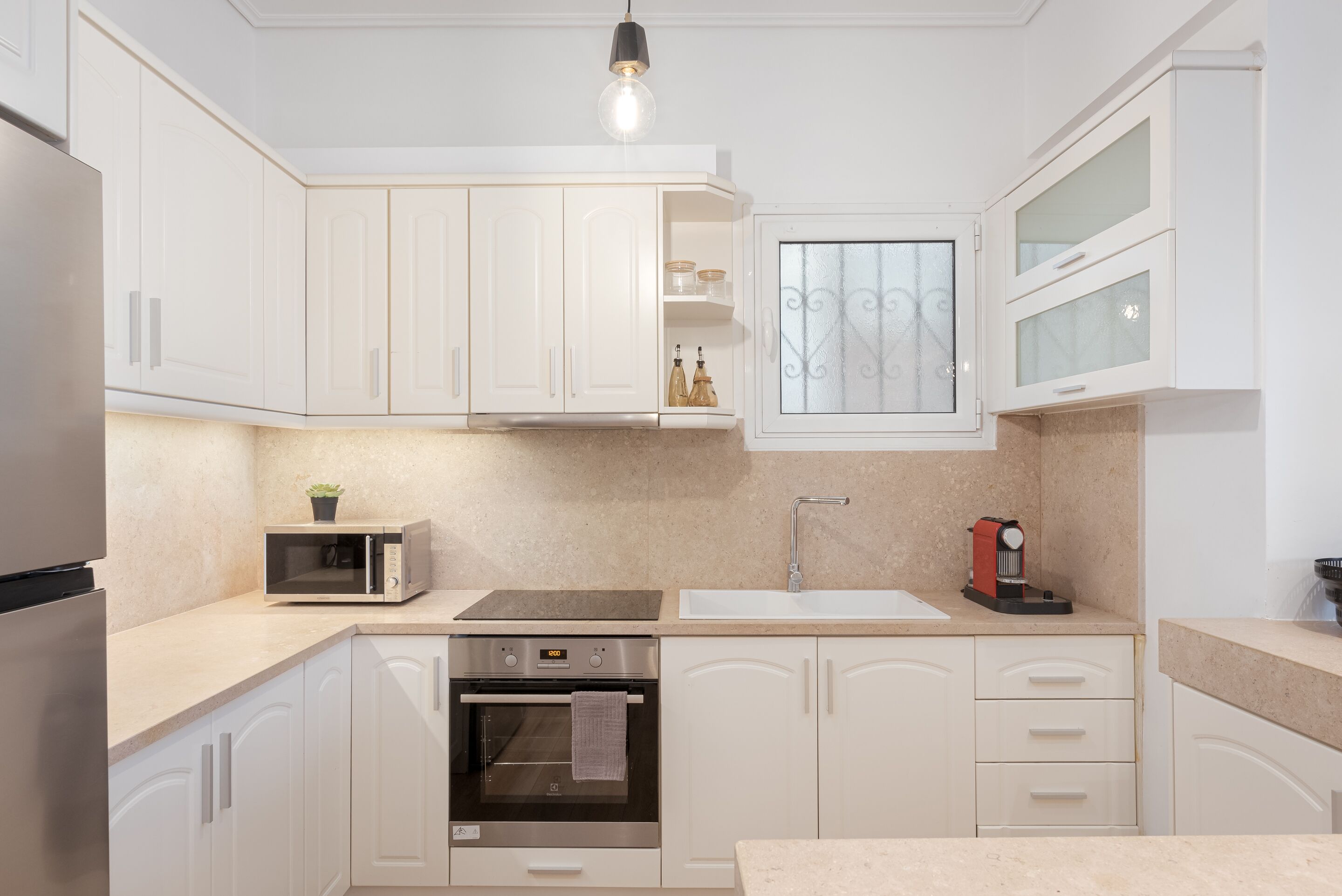 A modern kitchen with white cabinets, a built-in oven, a microwave, and a coffee maker.
