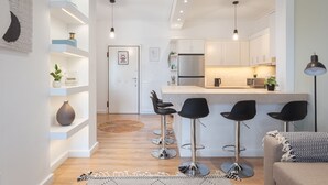 A modern kitchen with white cabinets, a central island with stools, and pendant lighting. - Glyfada Cozy Living (Glyfada)