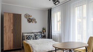 Une chambre à coucher moderne avec une armoire en bois, un lit agrémenté d’oreillers à motifs, une table ronde et une chaise jaune.