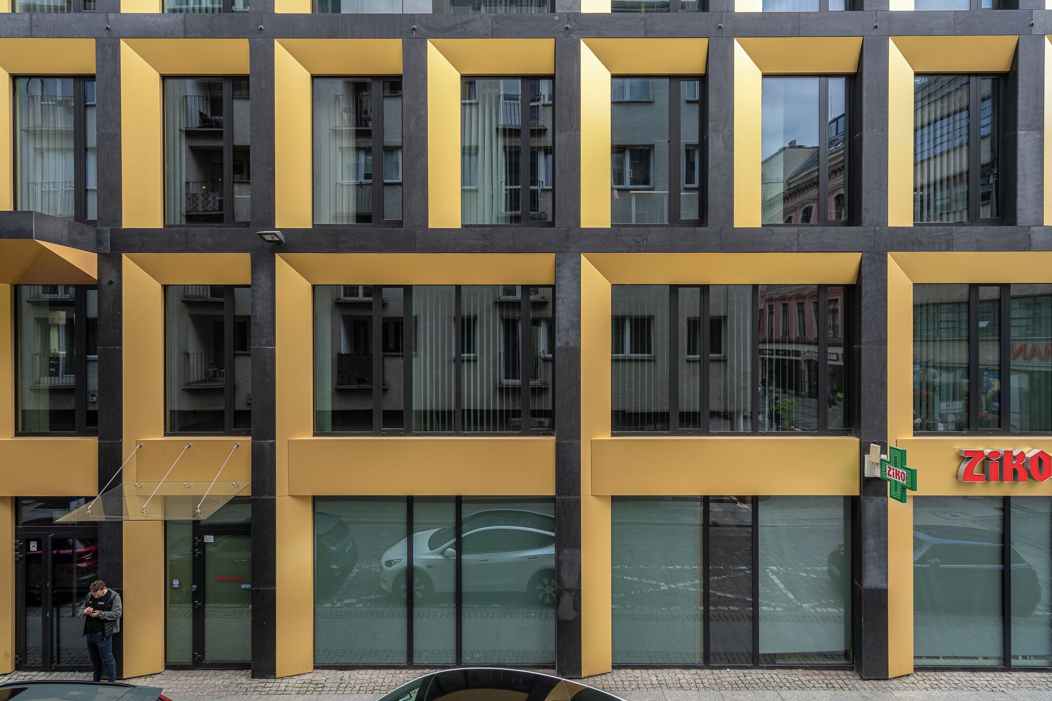 Um edifício moderno com fachada amarela, janelas grandes e entrada visível.