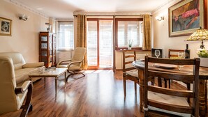 Un salon spacieux avec une table à manger en bois, un canapé et un fauteuil. On y trouve également un meuble avec des portes en verre et un tableau accroché au mur.