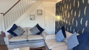 A living room with a beige sectional sofa, a coffee table with a vase of flowers, a staircase, and a wall with feather patterns. - 1 Regent Square (Rye)