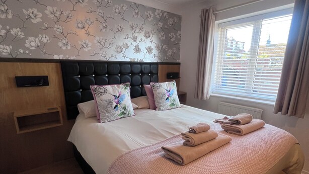 A neatly made bed with pillows and a blanket, a headboard, a bedside table, and a window with curtains. - 1 Regent Square (Rye)