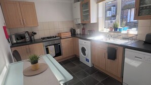 A compact kitchen with a gas stove, microwave, and dishwasher. There is a window with potted plants and a view of the outside. - 1 Regent Square (Rye)