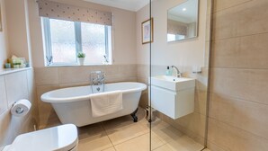 A bathroom with a freestanding bathtub, a toilet, a sink, and a window with a curtain. - 1 Regent Square (Rye)